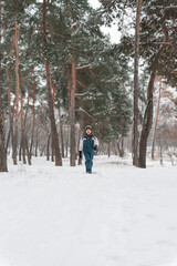 Boy in winter jumpsuit and multi-colored hat comes out snow-covered forest. Walk against of beautiful winter landscape