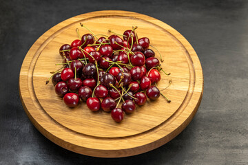 Ripe red cherry on wooden plate on gray background. Sweet fresh juicy organic cherries.