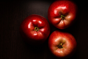 red juicy apples lie on a dark surface.