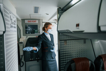 In protective gloves and mask. Young stewardess on the work in the passanger airplane