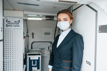 Fototapeta na wymiar In protective gloves and mask. Young stewardess on the work in the passanger airplane