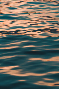 Rippled surface of blue sea water in sunset, orange and teal tones