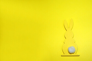 yellow wooden figure of an Easter bunny with a white tail on a yellow background top view. Easter Holiday