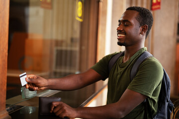 Young man buying a ticket for train with a credit card. Handsome smiling man going to a trip
