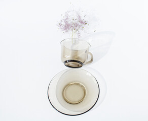 An empty coffee glass cup (mug) with a plate with a purple branch floating above on a white background. Minimalist creative concept of coffee and tea culture. Copy space. Flat lay.