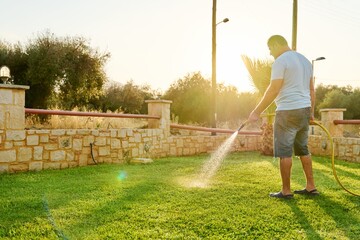 Man watering the lawn with a hose in the morning - Powered by Adobe