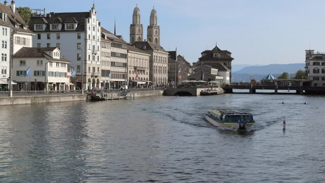 26.05.2021 zurich switzerland: large passenger ferry floating upstream towards camera, blue and white streetcar on left, dusk cloudless, blue sky, grossmünster, tourist attraction