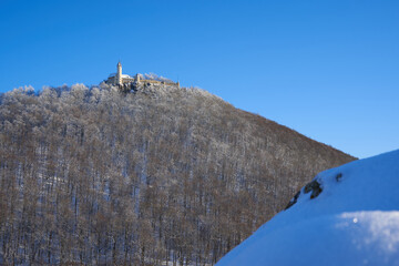 Castle also Stronghold (Teck) in winter on a clear evening with blue sky, many trees on the hill, big rock with snow in the foreground. Germany, Owen, Swabian alb.