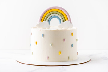 Birthday cake with white cream cheese frosting decorated with colorful mastic rainbow on the white...