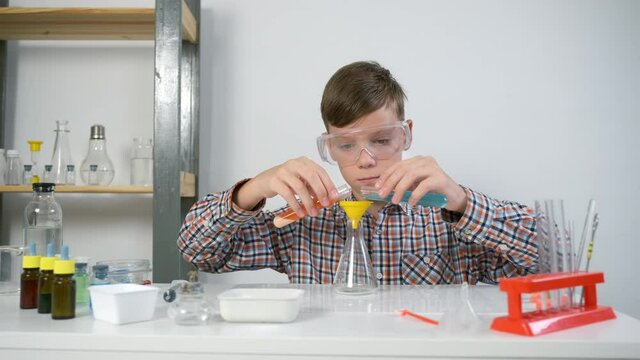 Teen boy in protective glasses is doing chemistry experiments with gas reaction. He is mixing soda, citric acid and blue and red liquid in flask. Online education, homeschooling and science concept.