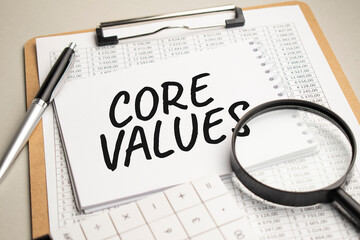 On the table are reports, a magnifying glass, a calculator, and a white notepad with the words Core Values. Business concept