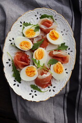 Italian salad. Boiled eggs with smoked ham and arugula on white plate. Dark wooden background