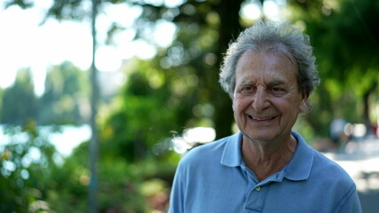 Smiling senior man walking outside in green path, one happy older person