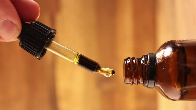 Vertical close-up shot of male hand taking a dropper with pure organic CBD cannabis oil.
