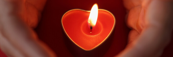 Women hands carefully protect candles in form of heart with burning fire