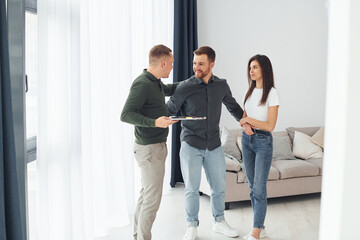 Salesman helps young couple in choosing an apartment. Conception of business and rent