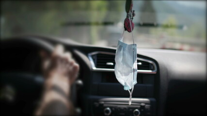 Person driving on road with covid surgical face mask hanging inside