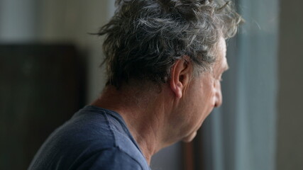 Pensive senior man standing by window looking outside. Thoughtful old person