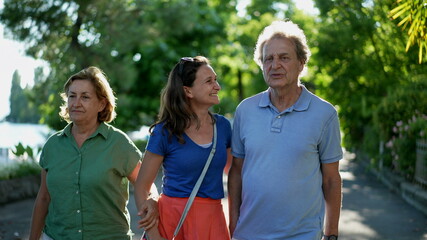 Parents walking with adult daughter together, family day walk outside laughing and smiling
