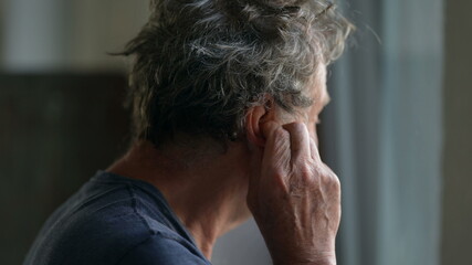 Older man touching ear scratching earlobe standing by window