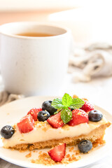 piece of strawberry and blueberry cheescake on plate and cup of tea served for breakfast at home, hotel or cafe. Dessert meal, sweet food . High quality photo