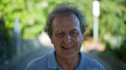 Happy senior man walking forward smiling. One older person walks in green urban city