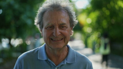 Happy senior man walking forward smiling. One older person walks in green urban city