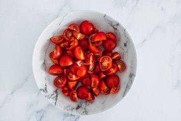 fresh ripe cherry tomatoes cut into cubes in marble bowl on marble tabletop, simple ingredients concept