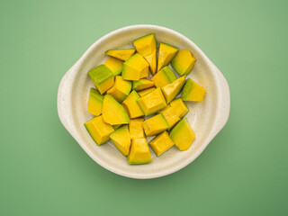 Top view of diced avocados in a ceramic bowl isolated on a green background