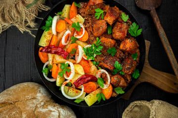 Stew with meat and vegetables in black iron dish. Traditional  gourmet goulash in a rustic kitchen....