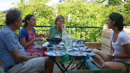 Family sitting at table during lunch outside in conversation during summer day