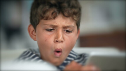 Child surprised reaction holding tablet. Boy WOW face emotion