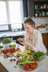 Young pregnant woman preparing healthy food with lots of vegetables at home and use a smartphone to look for some recipes. Healthy diet