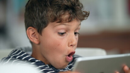 Child amazed reaction to content online holding tablet