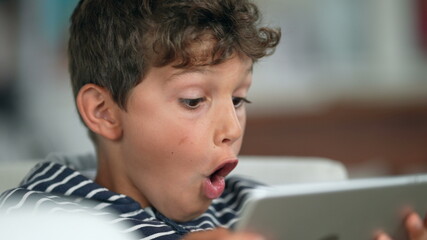 Child amazed reaction to content online holding tablet