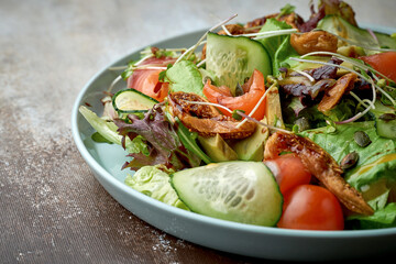 Salad with salmon, avocado, tomatoes and artichokes in a blue plate on a brown background