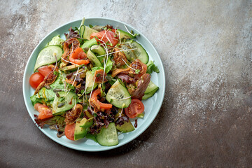 Salad with salmon, avocado, tomatoes and artichokes in a blue plate on a brown background