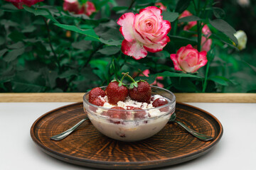 A delicious and healthy breakfast for two on a white table in the garden among blooming roses. Strawberries, cottage cheese, cream, honey