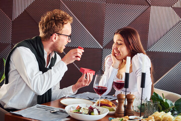 Young guy makes proposal to a woman. Indoors of new modern luxury restaurant
