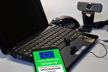 Covid-19 green passport. The digital green pass of the European Union on the screen of a smartphone with notebook, mouse, headphones and webcam. Safety concept at work with Green Pass for Covid-19