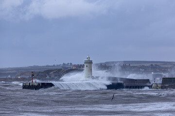 A scenic lighthouse at the Buckie, Moray, Scotland port entrance during a major storm with bid wave crashing on it under a grey stormy sky