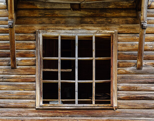 Window frame with broken glass in the wall of an old abandoned wooden house. The picture was taken in the village of Pervokrasnoe, in the Orenburg region