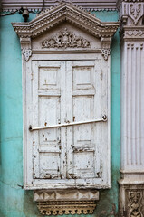 Carved wooden window with platbands and closed shutters, a fragment of the facade of an old building. The picture was taken in Russia, in the city of Orenburg
