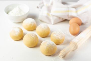 Six balls of dough covered with flour and two eggs are on the table next to a rolling pin and a towel. Preparing the dough for baking.	