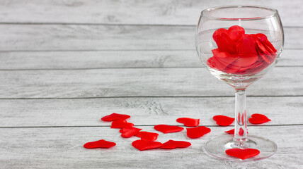 glass goblet with silk hearts on a wooden table. holiday concept. copy space.