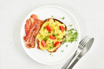 Scrambled eggs with microgreen, bacon and tomato slices on bread