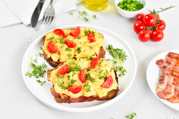 Scrambled eggs with microgreen, bacon and tomato slices on bread