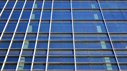 Commercial building close up in blue tone. Gigantic skyscraper from below. Architecture details of modern building amd glass facade. Business background on a beautiful sunny day. 