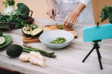 Young woman streaming online healthy food cooking lesson of green salad with vegetables and fruits - Focus on right hand