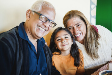 Happy latin child having fun eating with her grandparents at home - Focus on girl face